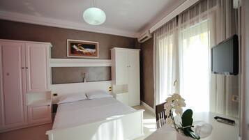 Un dormitorio con cama, armarios blancos, televisor montado y ventana con cortinas.
