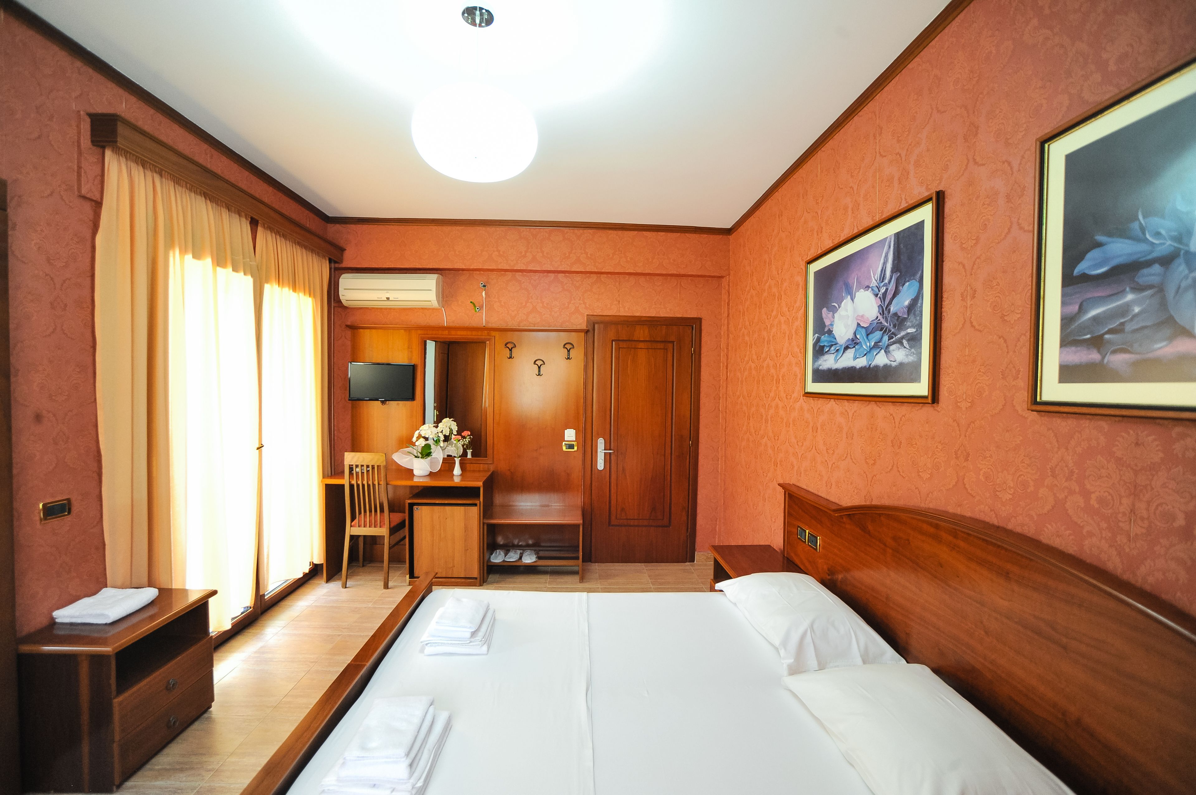 A hotel room with a bed, a desk, a chair, a wardrobe, and a large painting on the wall.