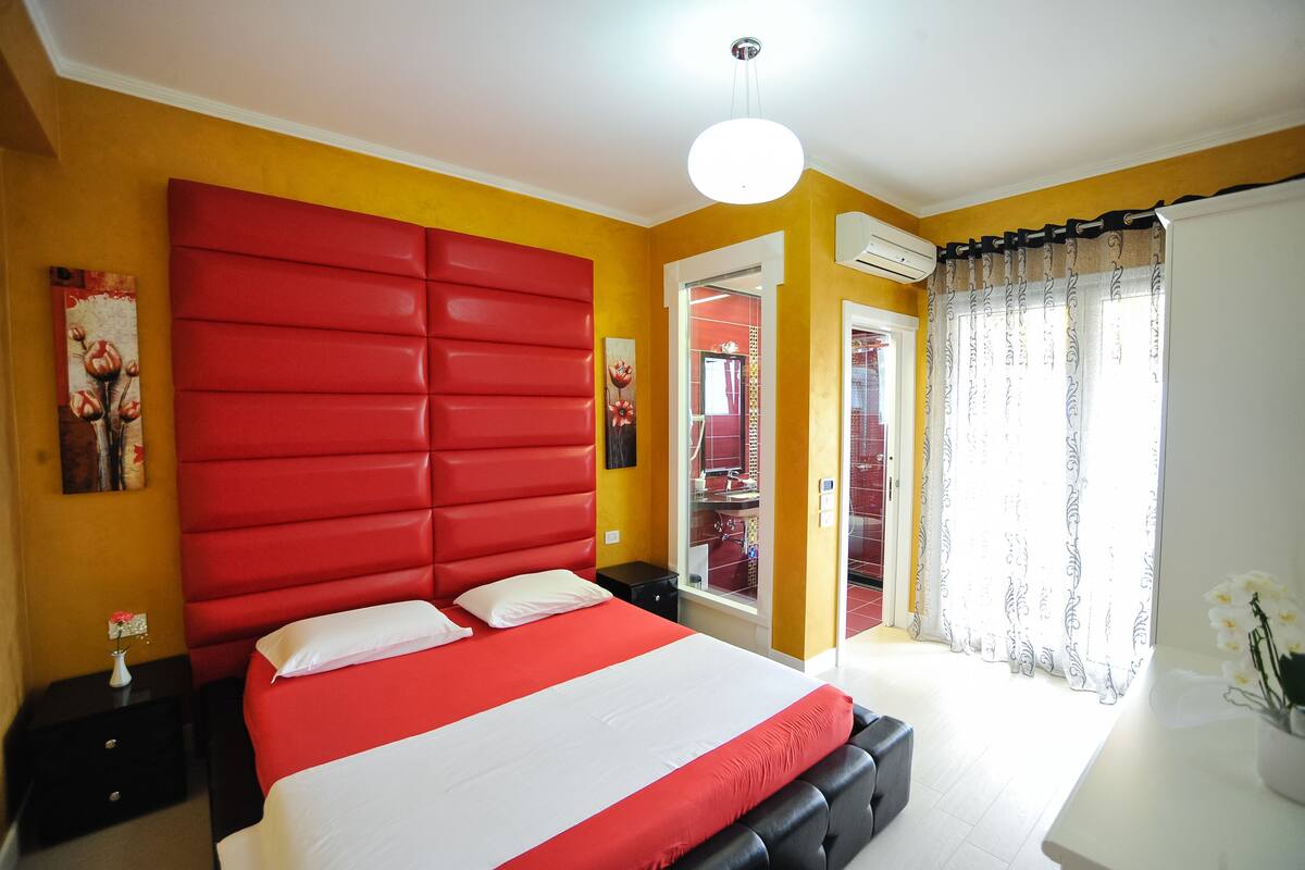 A bedroom with a red headboard, white bedding, and a white ceiling light.