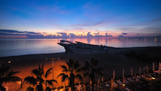 A beach with a pier extending into calm waters, palm trees, and beach chairs. - Hotel Iliria Internacional (Durrës)