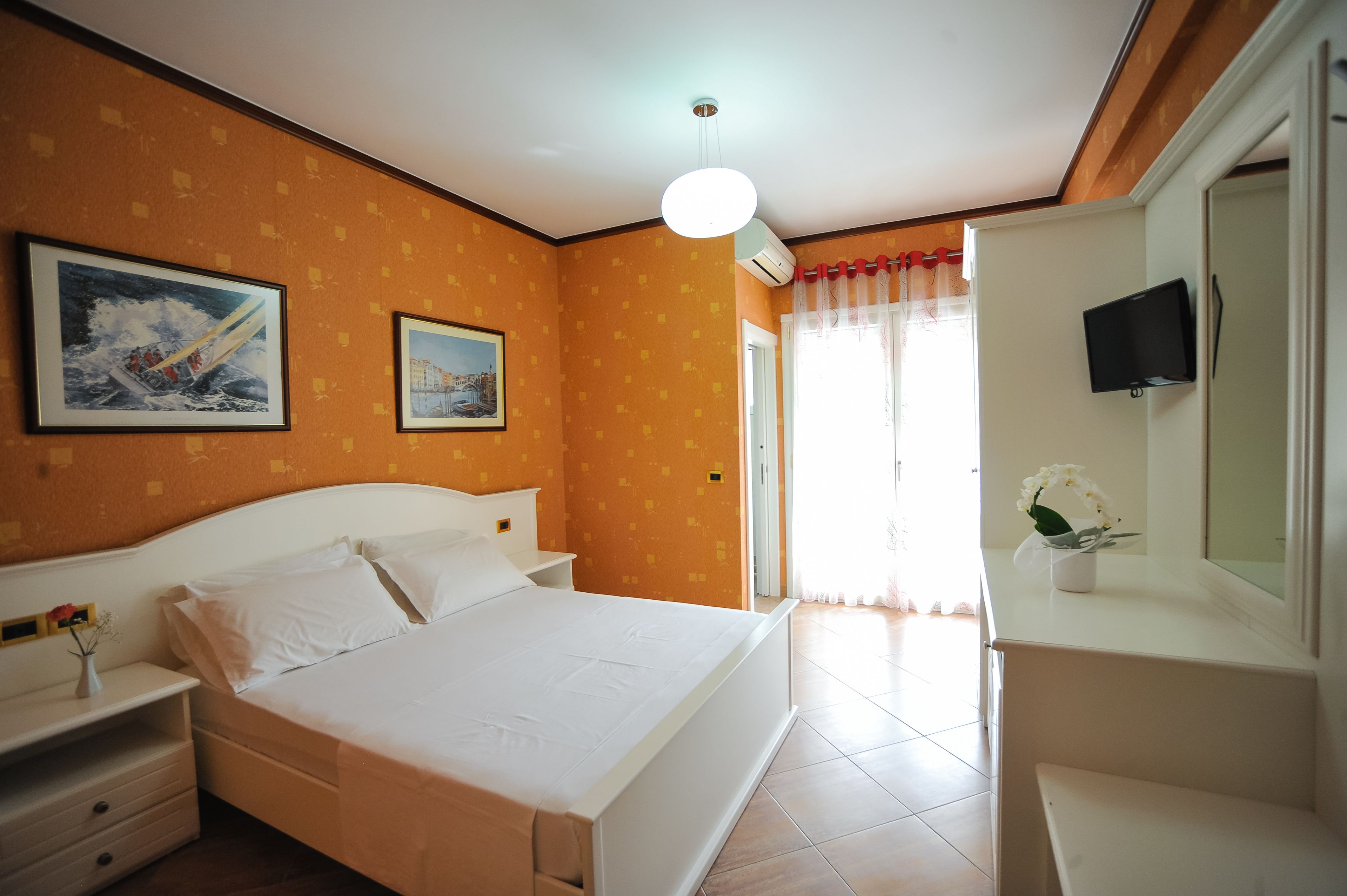 Una camera d'albergo con un letto, comodini, una TV e una finestra con tende.