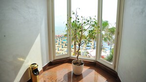A corner room with a potted tree, a trash bin, and a view of a beach with umbrellas. - Hotel Iliria Internacional (Durrës)