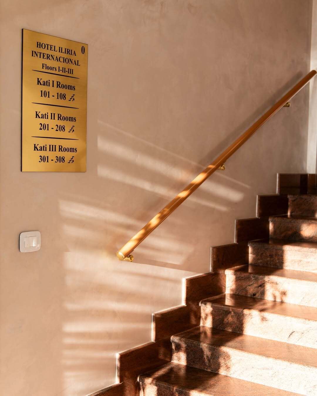 A staircase with a handrail and a sign indicating hotel rooms on Floors I-II-III.