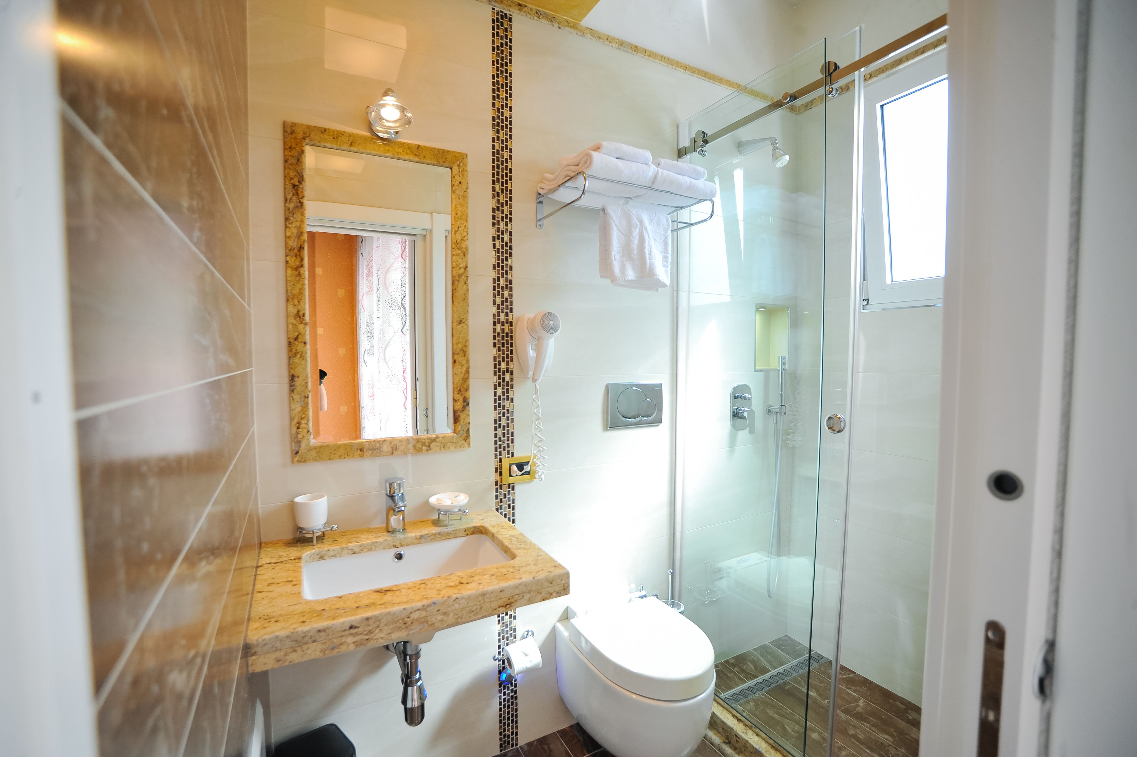 A bathroom with a marble sink, a toilet, a glass shower enclosure, and a mirror with a gold frame.