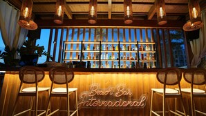 A bar area with wicker chairs, a neon sign reading "Beach Bar International," and shelves of bottles behind glass. - Hotel Iliria Internacional (Durrës)