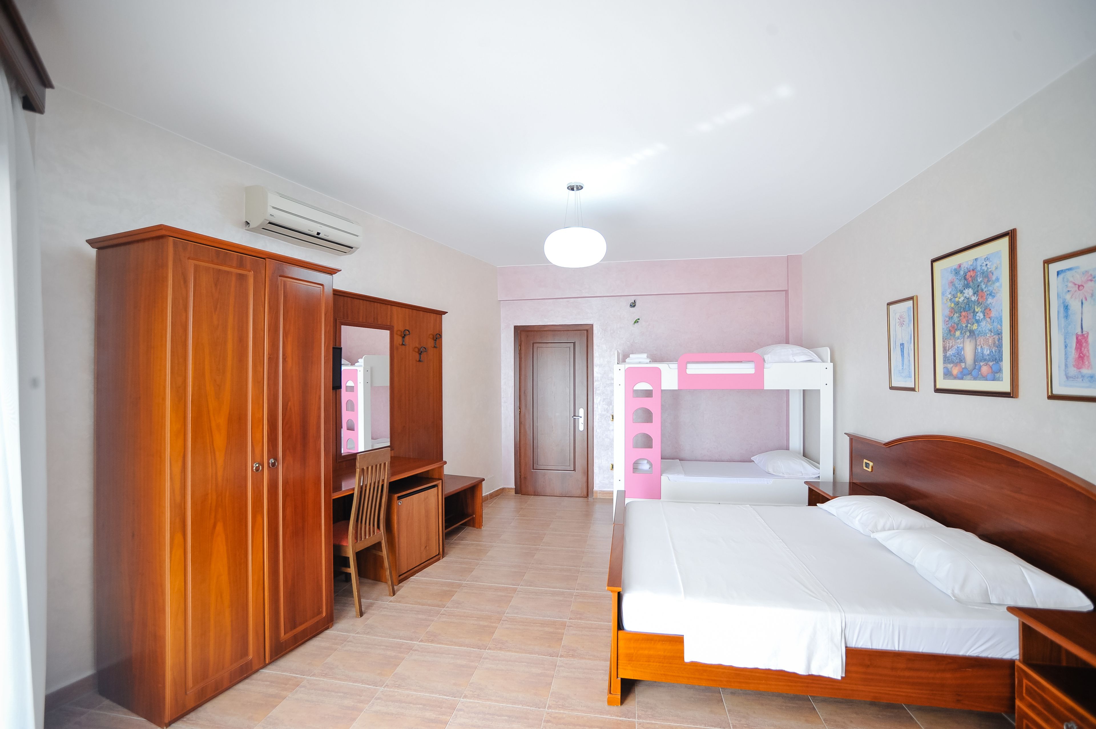 A bedroom with a wooden wardrobe, a desk, a bunk bed, and a bed.