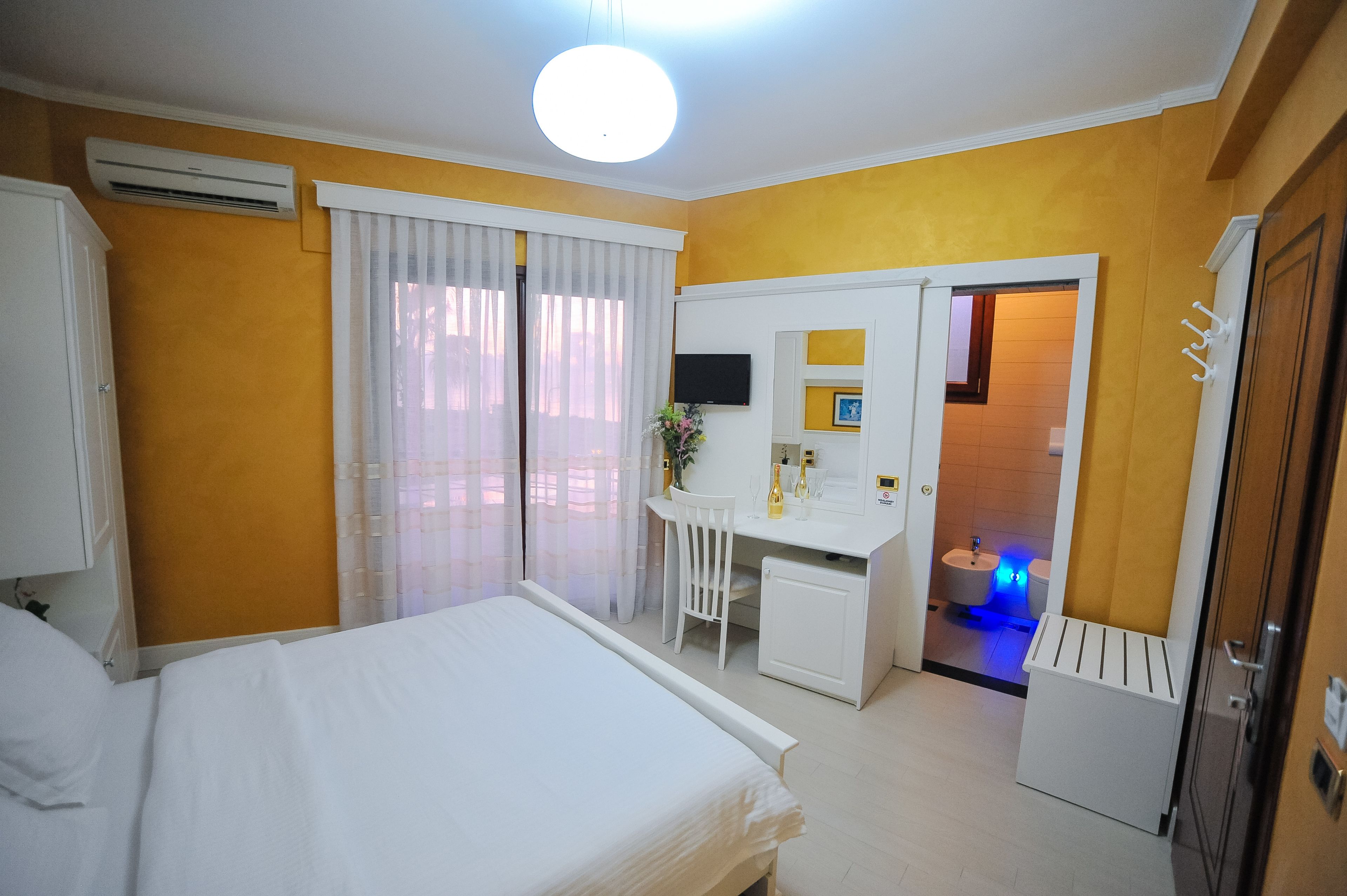 A hotel room with a bed, a desk with a chair, a television, and a bathroom visible through an open door.