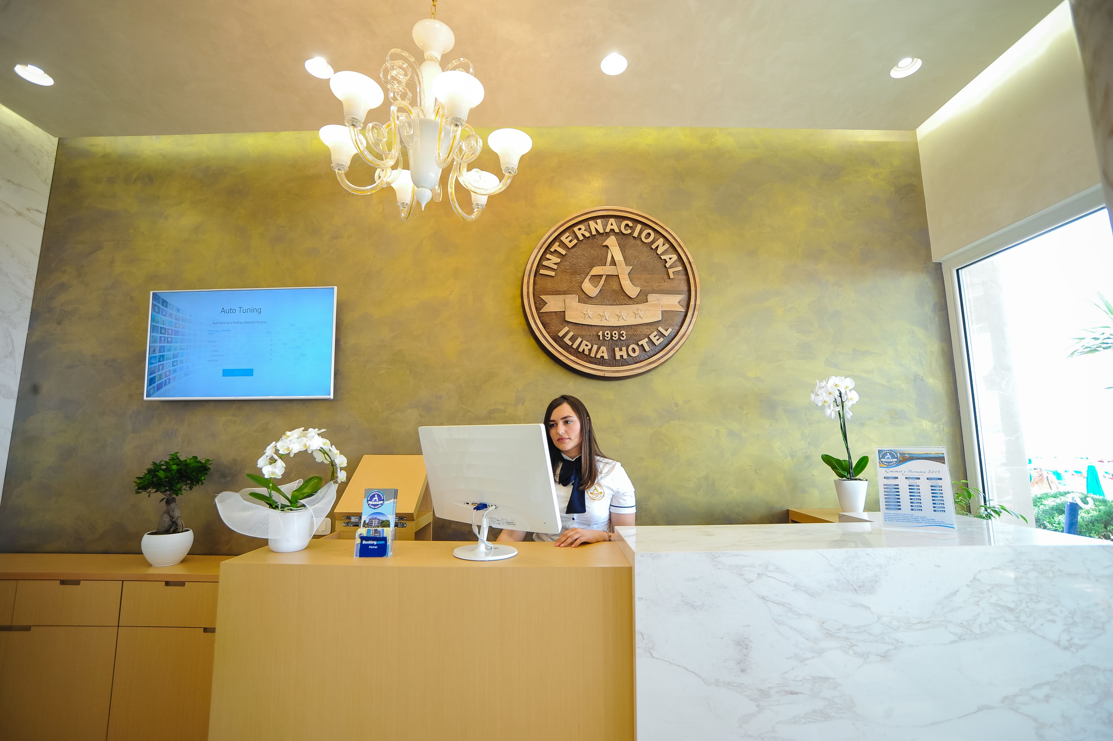 A reception desk with a computer, a chandelier, and a plaque on the wall.