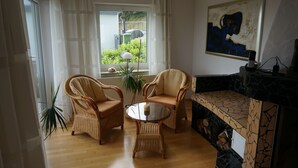 A living room with wicker furniture, a glass table, a fireplace, and a view of greenery outside. - Like new EFH for 6 pers. with garage in close proximity to Sorpesee (Langscheid)