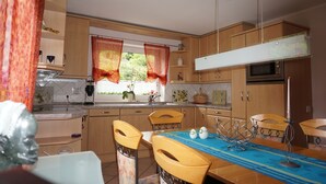 A compact kitchen with wooden cabinets, a microwave, and a dining area with a table and chairs. - Like new EFH for 6 pers. with garage in close proximity to Sorpesee (Langscheid)