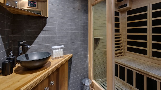 Un baño moderno con tocador de madera, un lavabo negro grande y una sauna con bancos de madera.