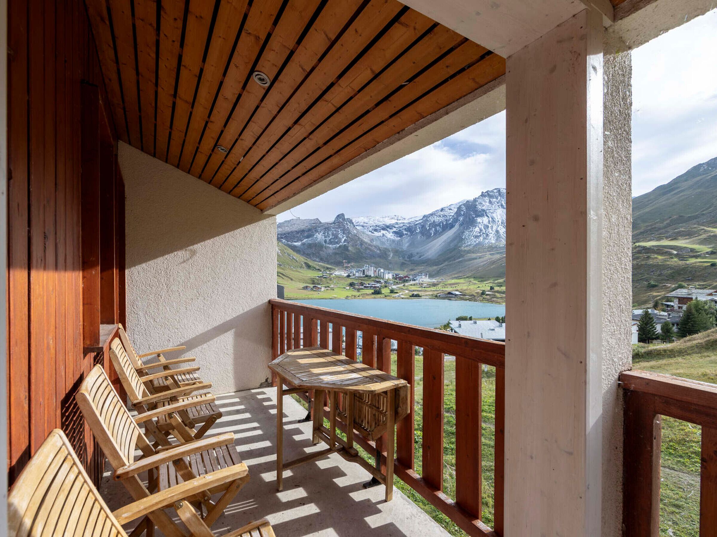 Un balcón con mobiliario de madera con vistas a un paisaje montañoso y un lago.