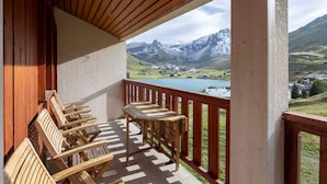 Un balcón con mobiliario de madera con vistas a un paisaje montañoso y un lago.