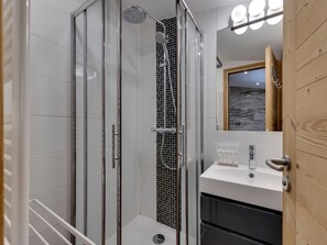 A modern bathroom with a glass-enclosed shower, a white sink, and a wooden door.