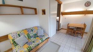 Une petite pièce accueillante, avec un canapé en bois, une petite table et un coin cuisine à l’arrière-plan.