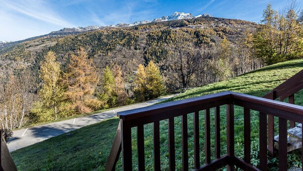 Une vue sur les montagnes depuis une terrasse en bois, avec un ciel dégagé.