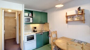 Une cuisine compacte équipée d’un four à micro-ondes, d’un four traditionnel et d’un évier, avec des meubles de couleur verte, une table à manger en bois et un ventilateur de plafond.