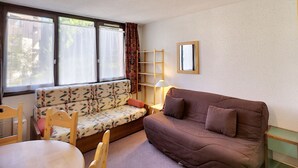 Un espace de vie compact comprenant un canapé, une table à manger et une fenêtre avec des rideaux.