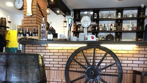 A bar area with a large wooden barrel, a vintage-style wall clock, and shelves stocked with various bottles and glasses. - Hotel Beer House (Sarandë)