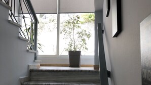 A staircase with a potted plant at the top, leading to a room with a large window and a ceiling light. - Hotel Beer House (Sarandë)