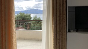A room with a balcony, a TV, and a view of a lake and mountains. - Hotel Beer House (Sarandë)