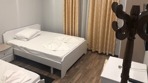 A bedroom with a white bed, a wooden floor, a bedside table, a lamp, and a window with curtains. - Hotel Beer House (Sarandë)