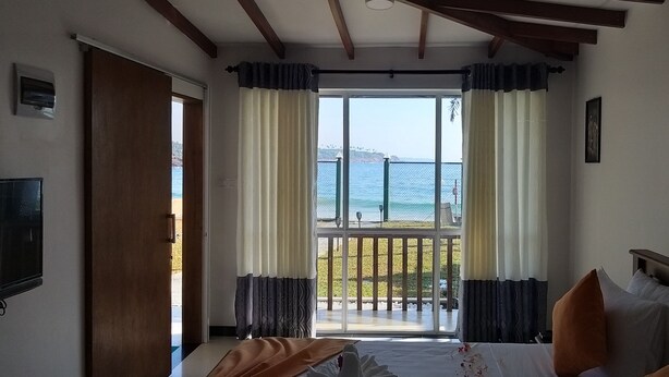 A hotel room with a bed, a TV, and a balcony with a view of the sea. - The Bay Beach (Tangalle)