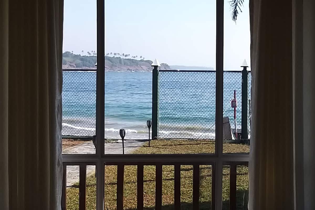 A view from a balcony with a metal railing, overlooking a body of water and a distant shoreline with trees and a hill.