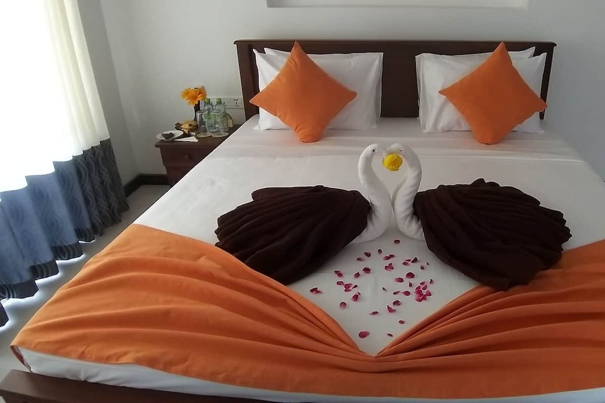 A neatly made bed with orange and white bedding, two orange pillows, and a decorative swan made of towels.