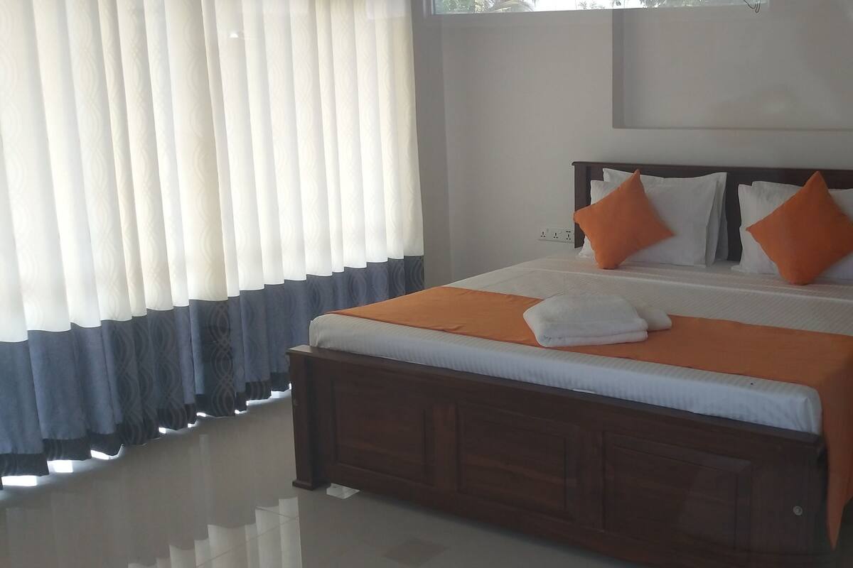 A neatly made bed with an orange blanket and pillows, a wooden headboard, and a white wall with a framed picture.