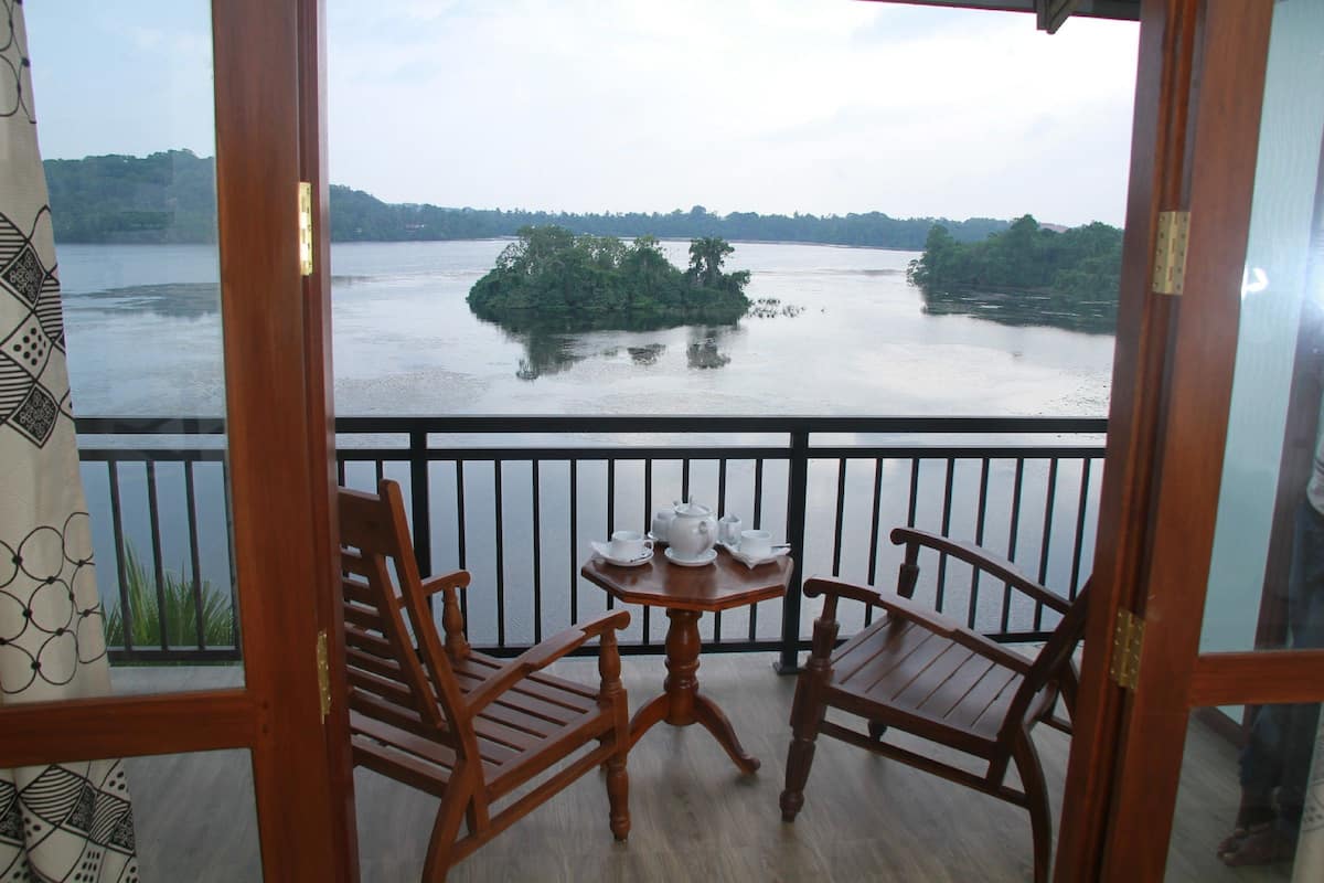 A balcony with two wooden chairs and a small table, overlooking a calm river with a small island.