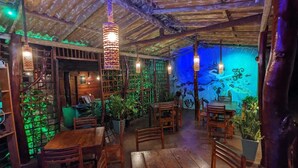 Un comedor interior con mesas y sillas de madera, luces colgantes y un mural en la pared.