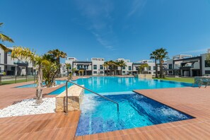 Un hotel moderno con piscina, palmeras y un cielo azul despejado.