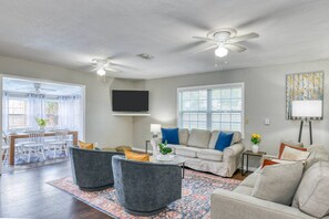 A living room with a sofa, two armchairs, a TV, and a dining area with chairs and a table.