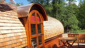 Una cabaña de madera con techo curvo, puerta de vidrio y una terraza con mesa y sillas.