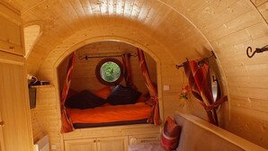 Interior acogedor de una cabaña con techo de madera, una cama con cortinas, un sofá y una mesa.