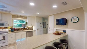 A modern kitchen with a large island, stainless steel appliances, and a flat-screen TV mounted on the wall. - Driftwood 4 bedrooms, 3 bathrooms (Jekyll Island)