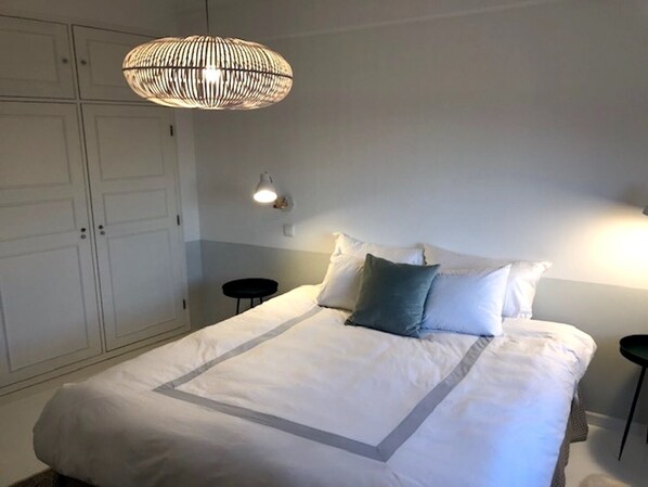 A bedroom with a large bed, a hanging light fixture, a wall-mounted lamp, and a wardrobe.