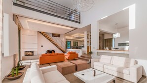 Un vaste espace de vie avec un escalier, des canapés blancs et, au fond, une cuisine moderne.