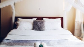 Un lit à baldaquin, avec une literie blanche et deux serviettes enroulées ornées d’une rose verte.