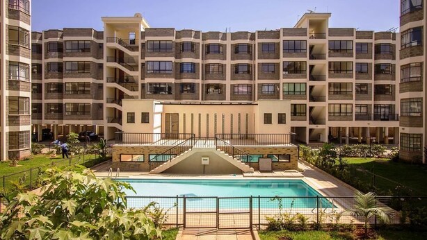 Un hôtel à plusieurs étages doté d’une cour intérieure où se trouve une piscine, le tout entouré d’une végétation luxuriante et d’une pelouse bien entretenue.