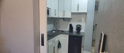 A compact kitchen with white cabinets, a black countertop, a sink, a coffee maker, and a dishwasher.