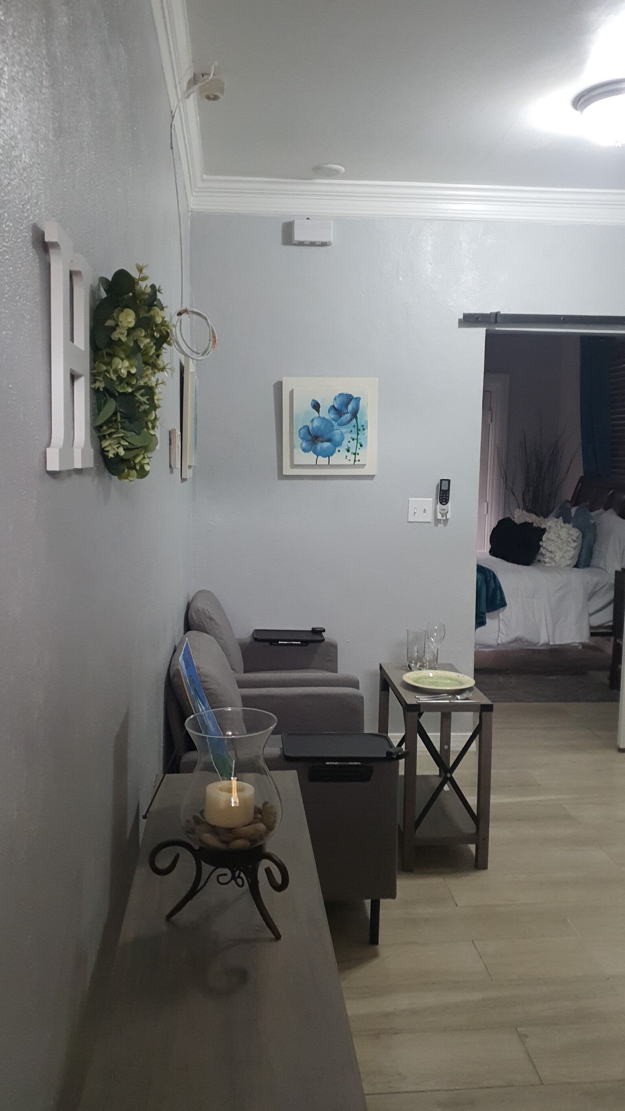 A living room with a grey sofa, a small table with a candle, and a painting of blue flowers on the wall.
