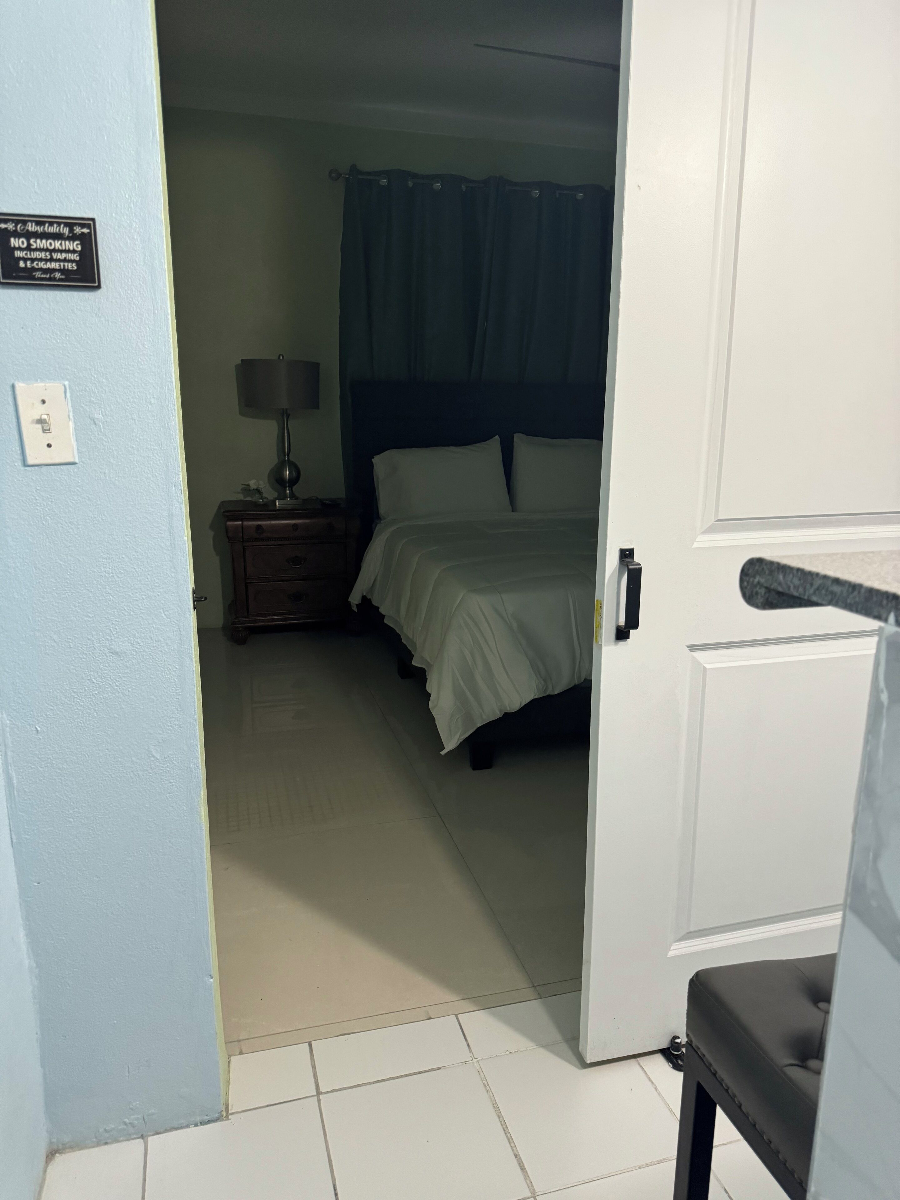A hotel room with a bed, a nightstand with a lamp, and a sign indicating no smoking.