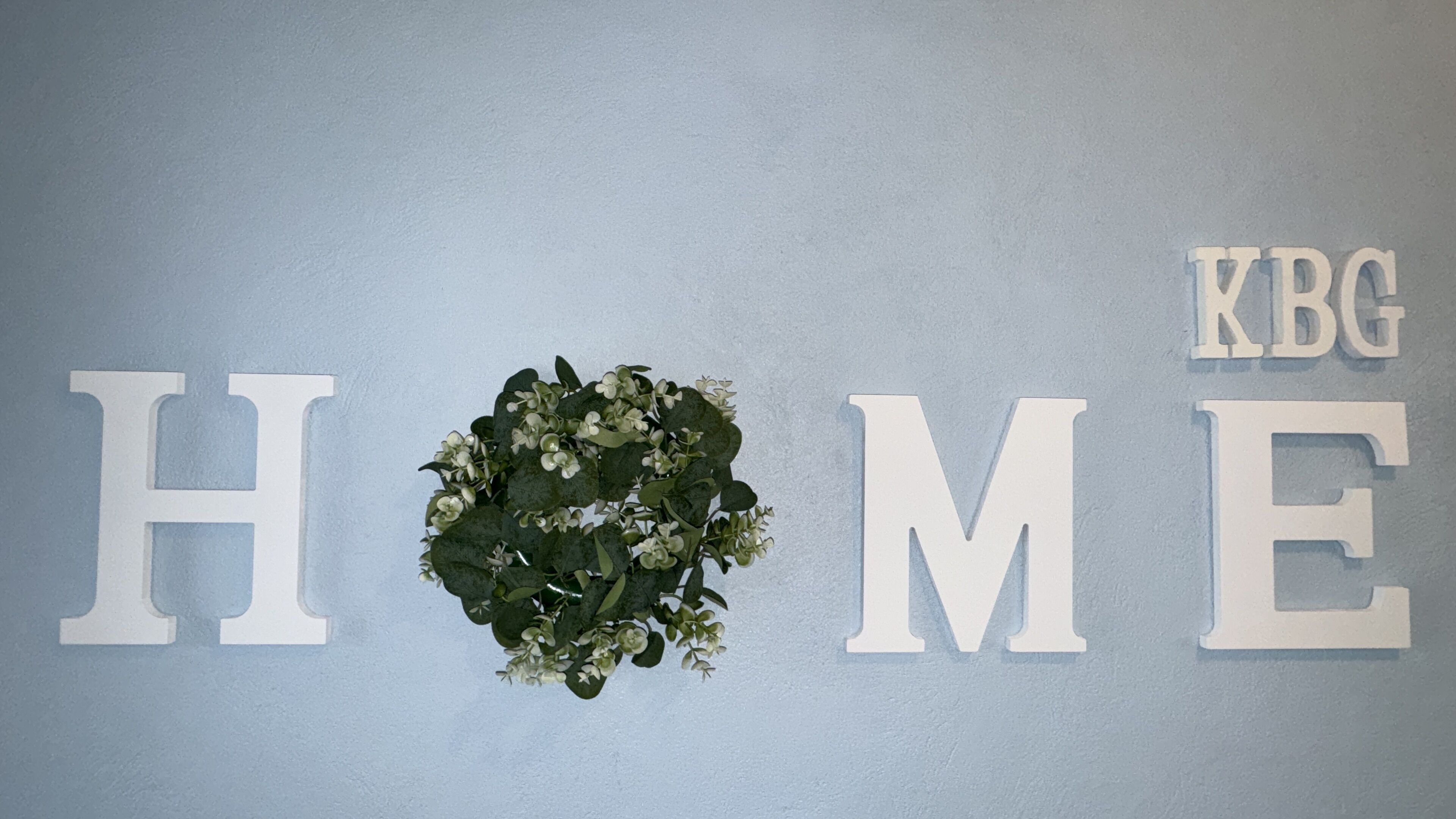 A wall with the words "HOME" and "KBG" in large letters, with a wreath in the center.