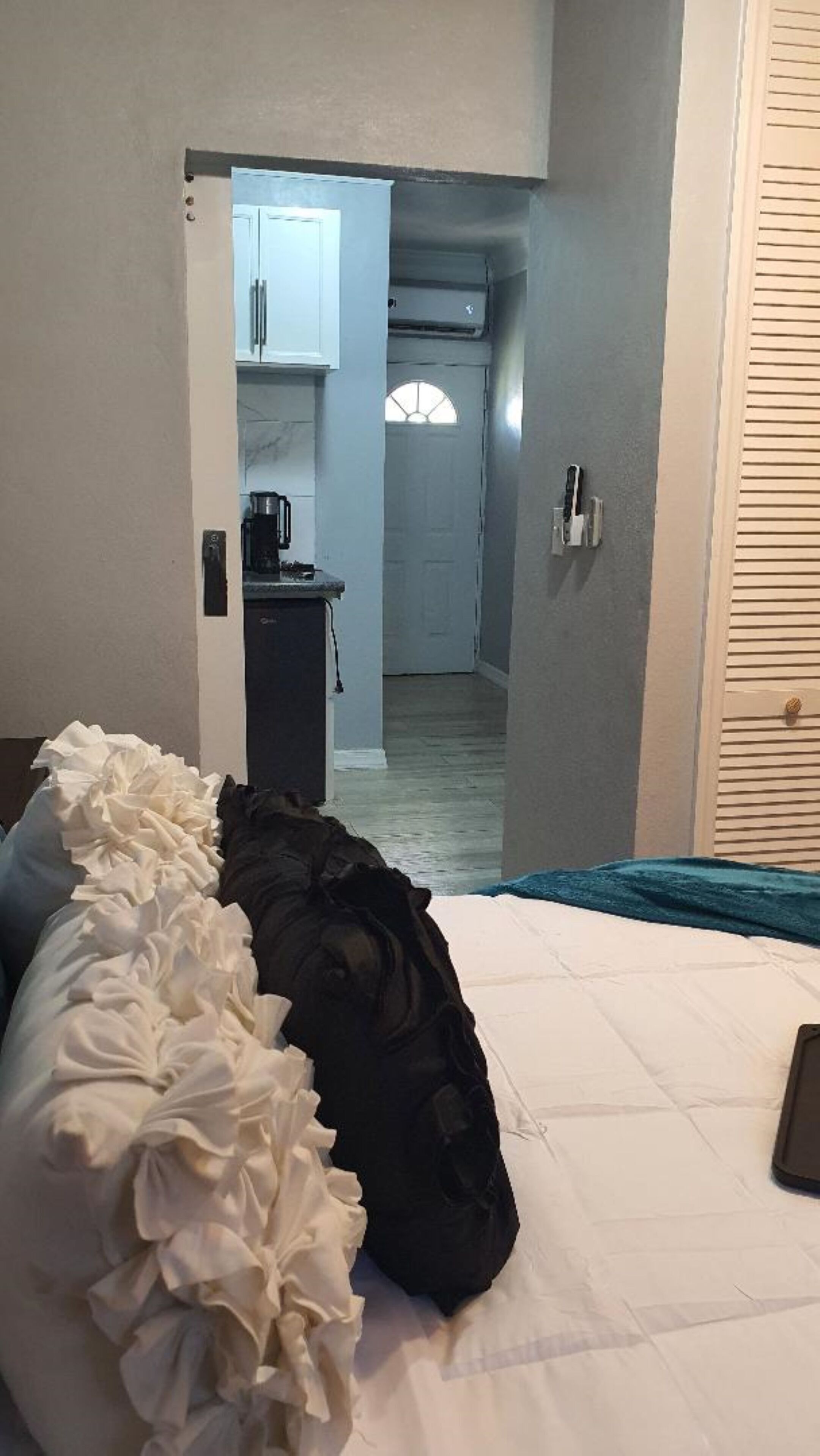 Ett hotellrum med en säng, ett sängbord, en kaffebryggare och utsikt över ett kök och en hall.