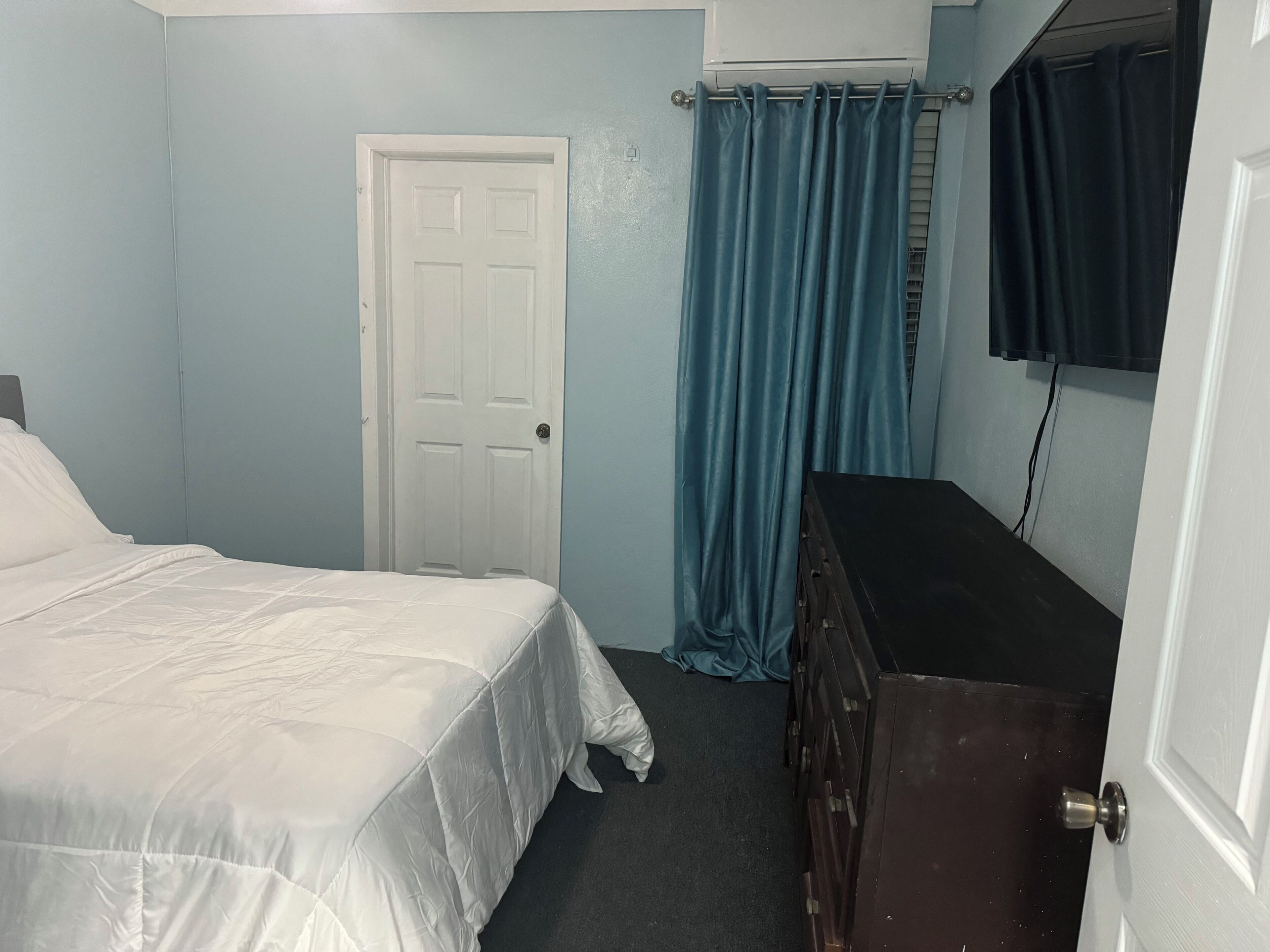 A bedroom with a bed, a dresser, a door, and a curtain.