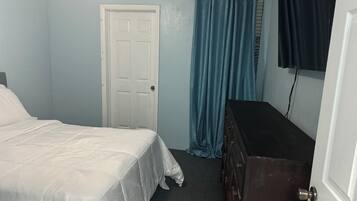 A bedroom with a bed, a dresser, a door, and a curtain.