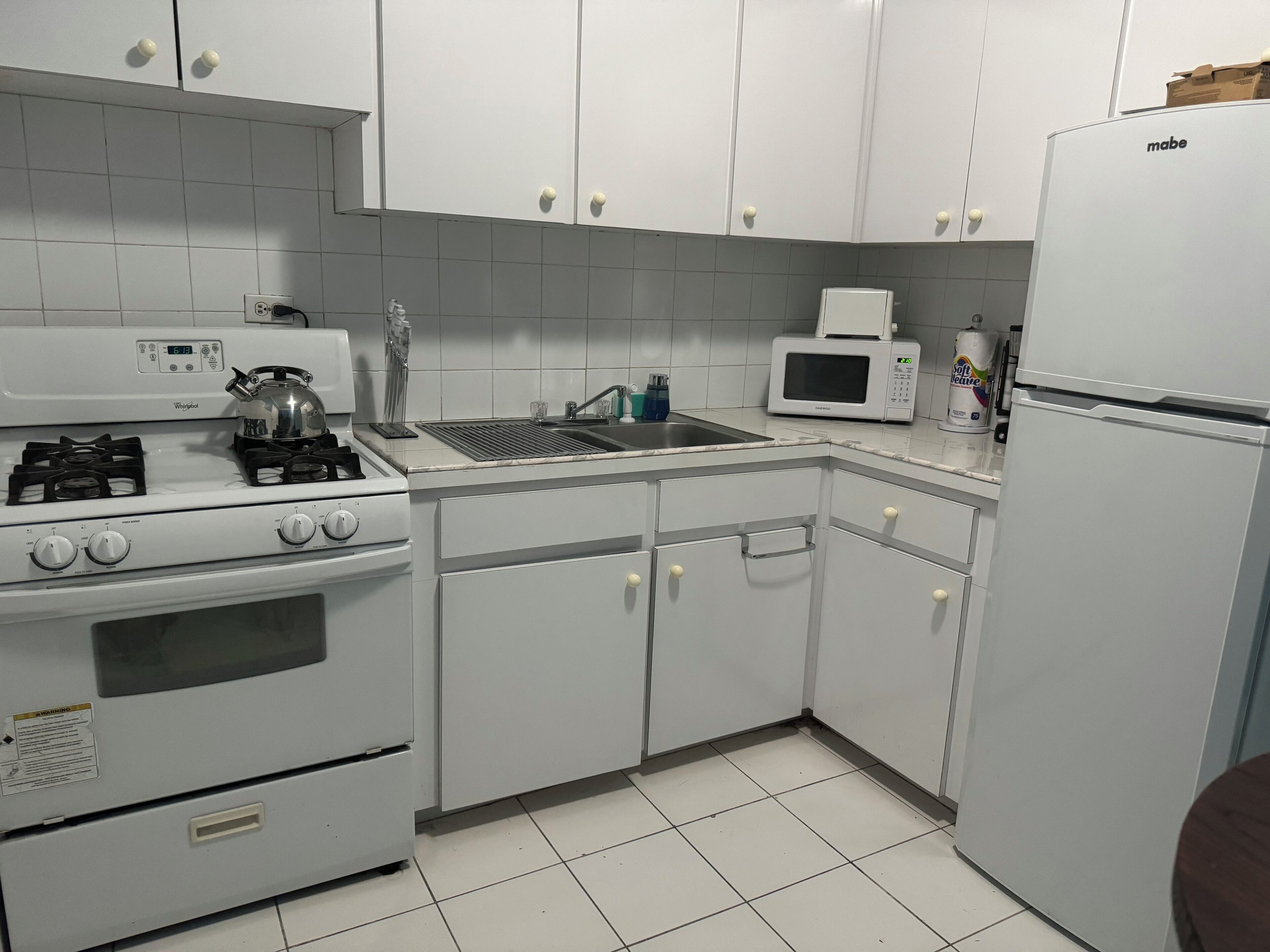 Una cocina con armarios blancos, estufa, microondas y refrigerador.