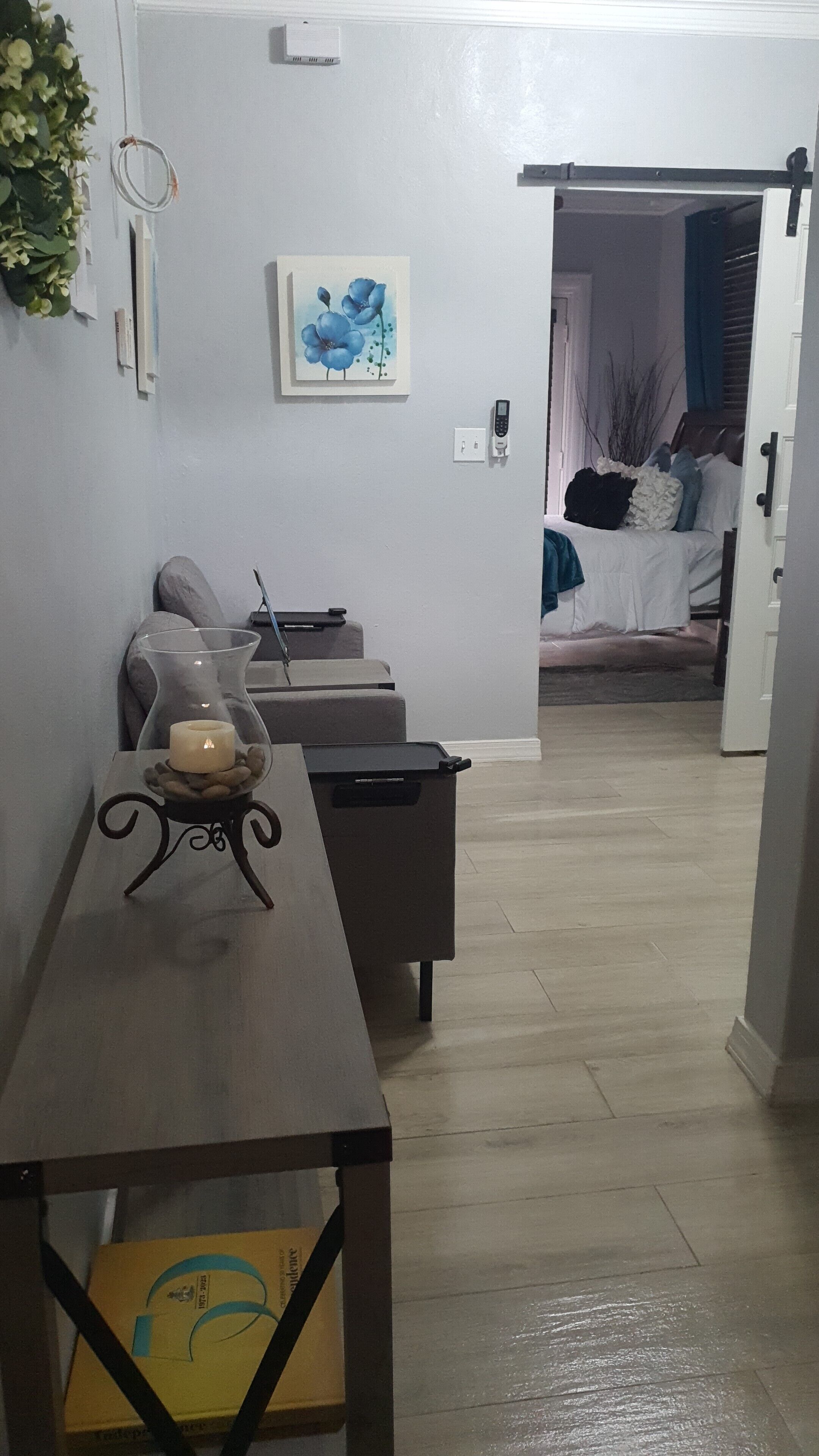 Ein Wohnzimmer mit einer Couch, einem Couchtisch mit einer Kerze, einem Gemälde und einem Bett im Hintergrund.